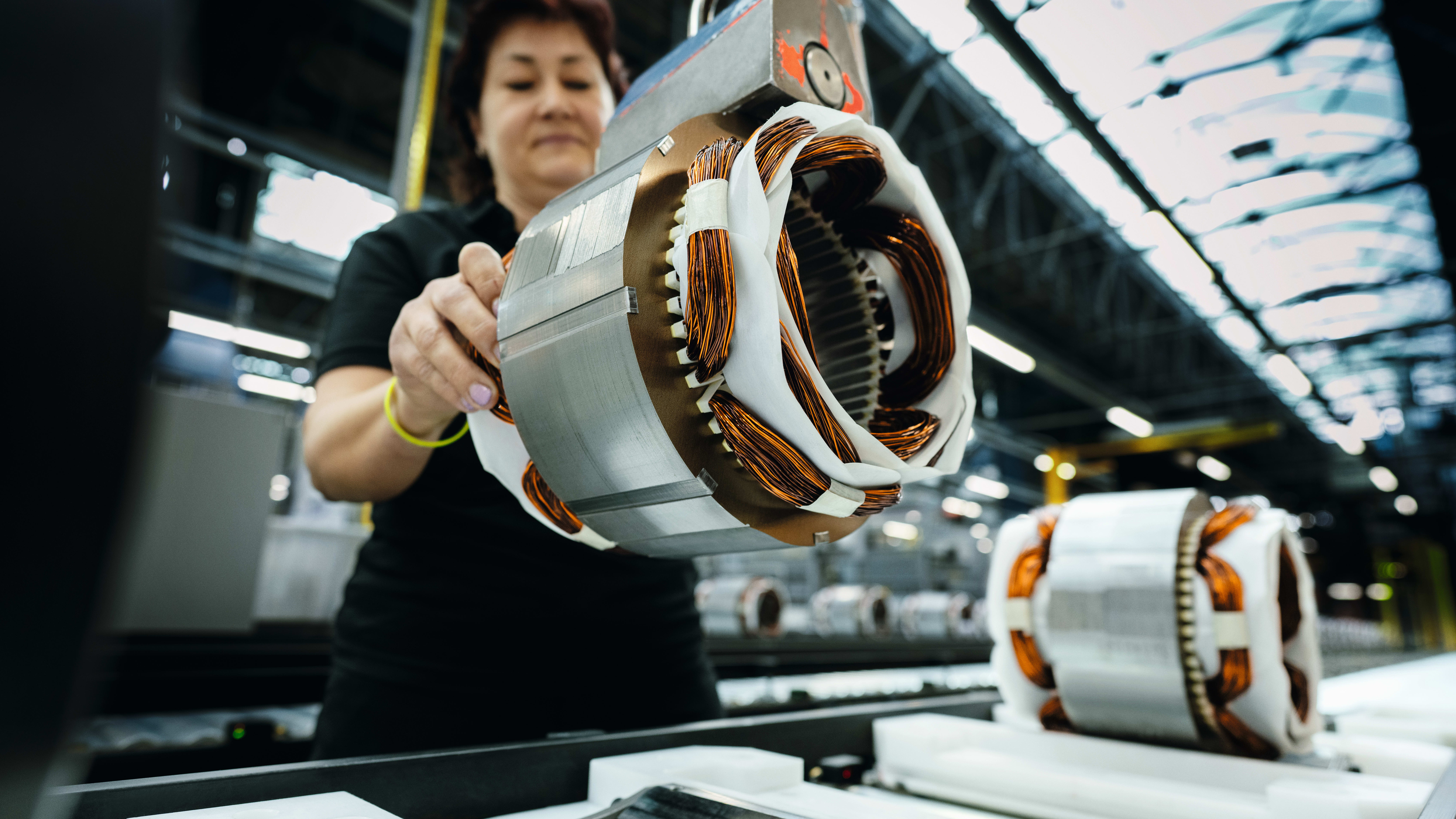 Worker holding a partially assembled electric motor rotor with copper coils in a factory. Worker holding a partially assembled electric motor rotor with copper coils in a factory.